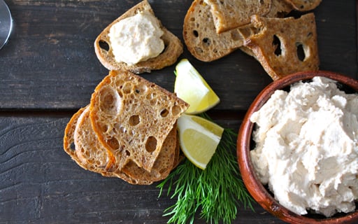 taramasalata in a terra cotta bowl next to sourdough bread with lemons and dill