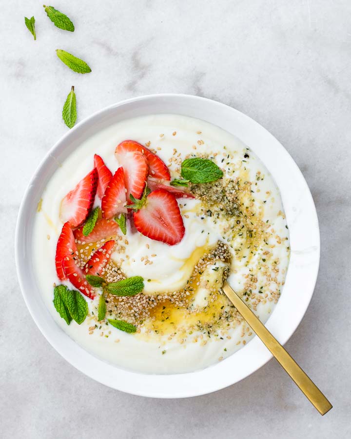 Raw milk yogurt in a bowl with strawberries, honey, mint and sesame seeds.