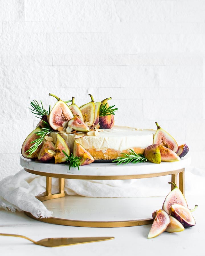 Fig tart on a marble cake stand garnished with figs, rosemary and sliced almonds.