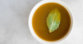 Bone Broth in a white bowl garnished with bay leaf