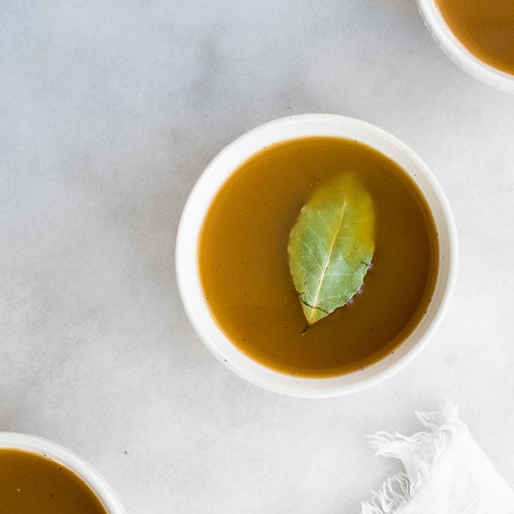 Beef bone broth in a bowl with a bay leaf.