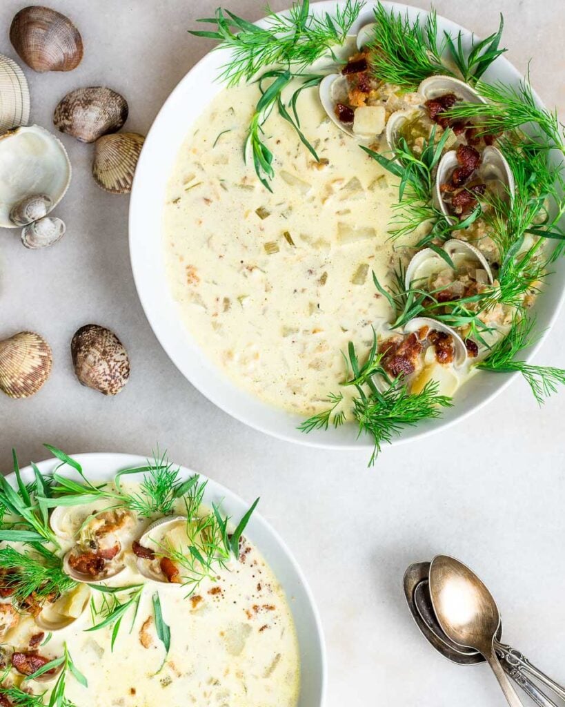 Two bowls of Main-style clam chowder made with fresh clams garnished with dill, tarragon and bacon.