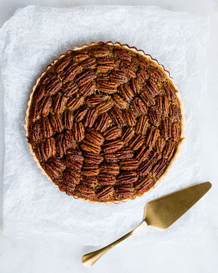 Maple pecan pie sitting on waxed paper with a pie server