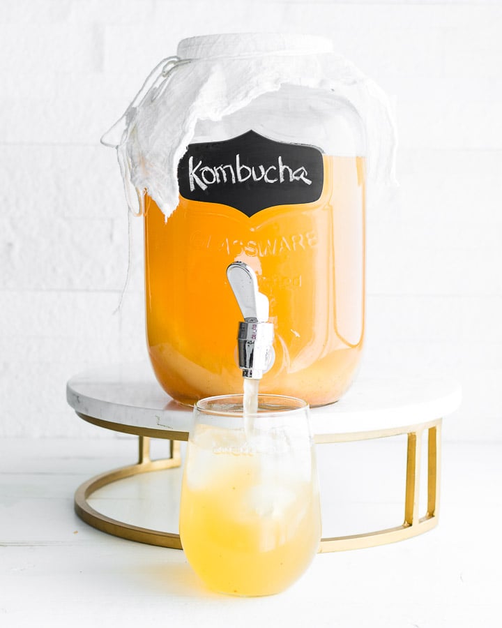 a jar of continuous brew kombucha on a marble stand, filling a cup with ice