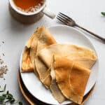 sourdough rye crepes on a white plate with a fork and cup of tea