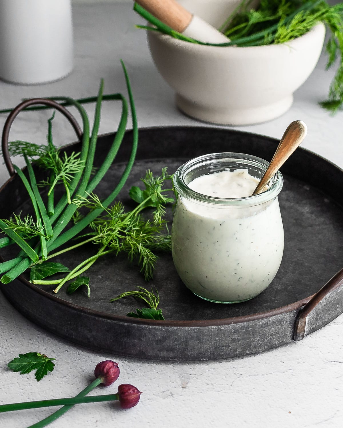 Kefir Ranch dressing in white jar on metal tray with fresh herbs on tray.
