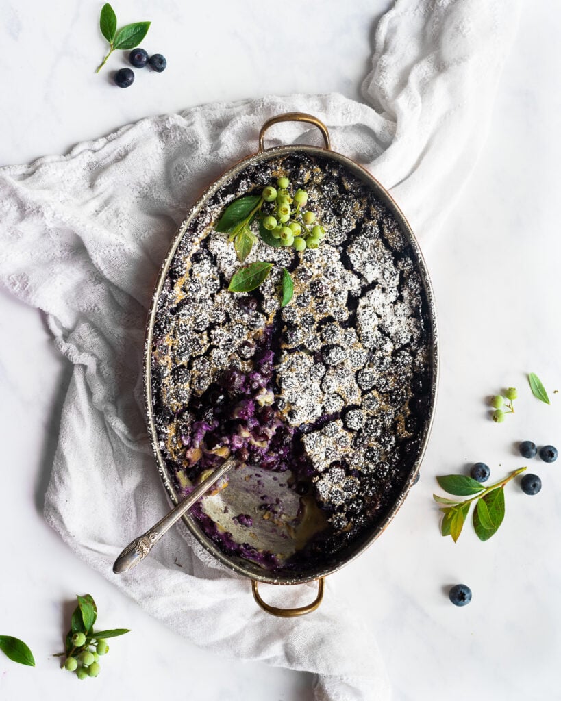 Blueberry clafoutis in a copper baking dish, dusted with powdered sugar and garnished with fresh blueberries,