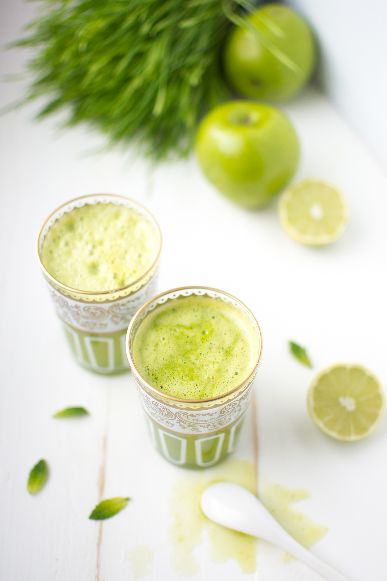 Super Green Morning Tonic in glass with apples, lime and wheatgrass in background
