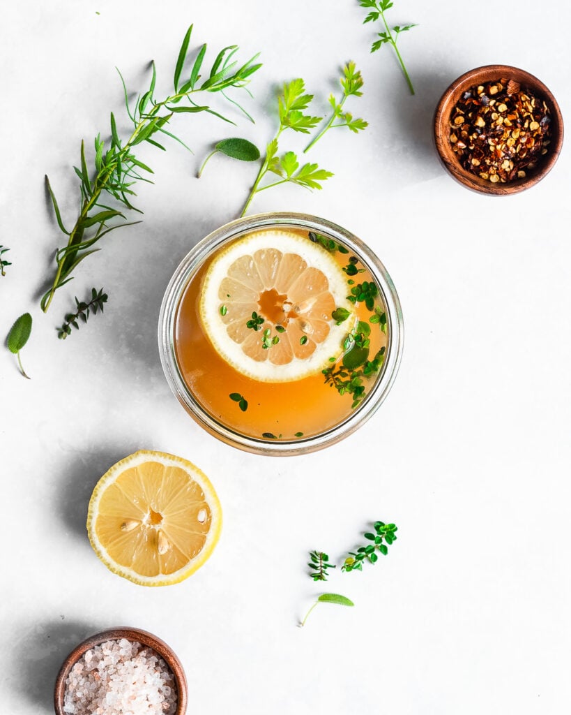 Turkey bone broth in a glass jar, garnished with lemon and fresh herbs.