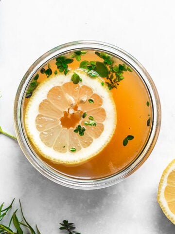 close up of turkey bone broth garnished with herbs and lemon