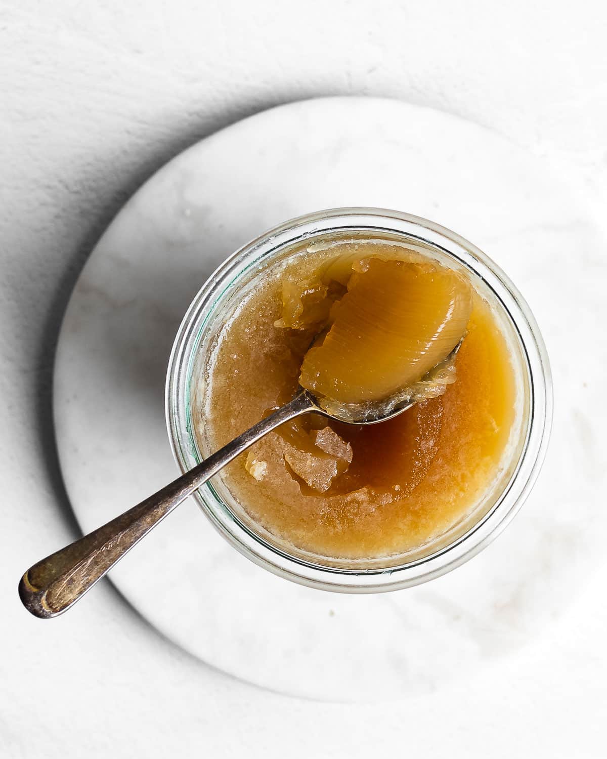Gelatinous chicken bone bone broth in a glass jar with a spoon on a white background.