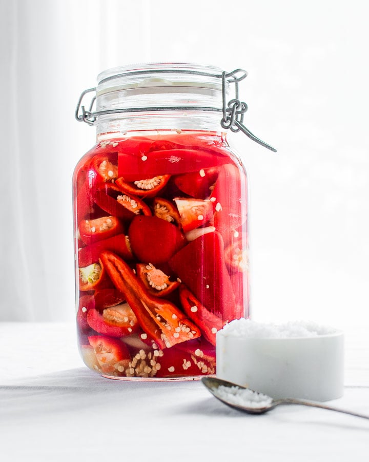 Ripe, red jalapeños, garlic and cherry bomb peppers fermenting in a glass jar for hot sauce