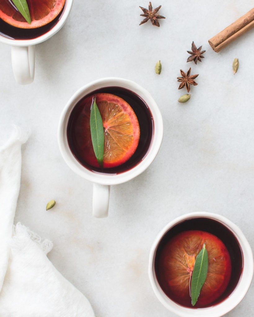 Three cups of mulled wine garnished with orange, bay leaf, and cinnamon.