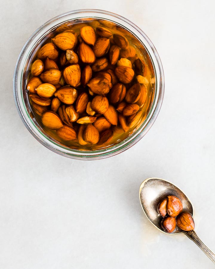 Apricot kernels sit in a glass  jar of noyaux (homemade almond extract).