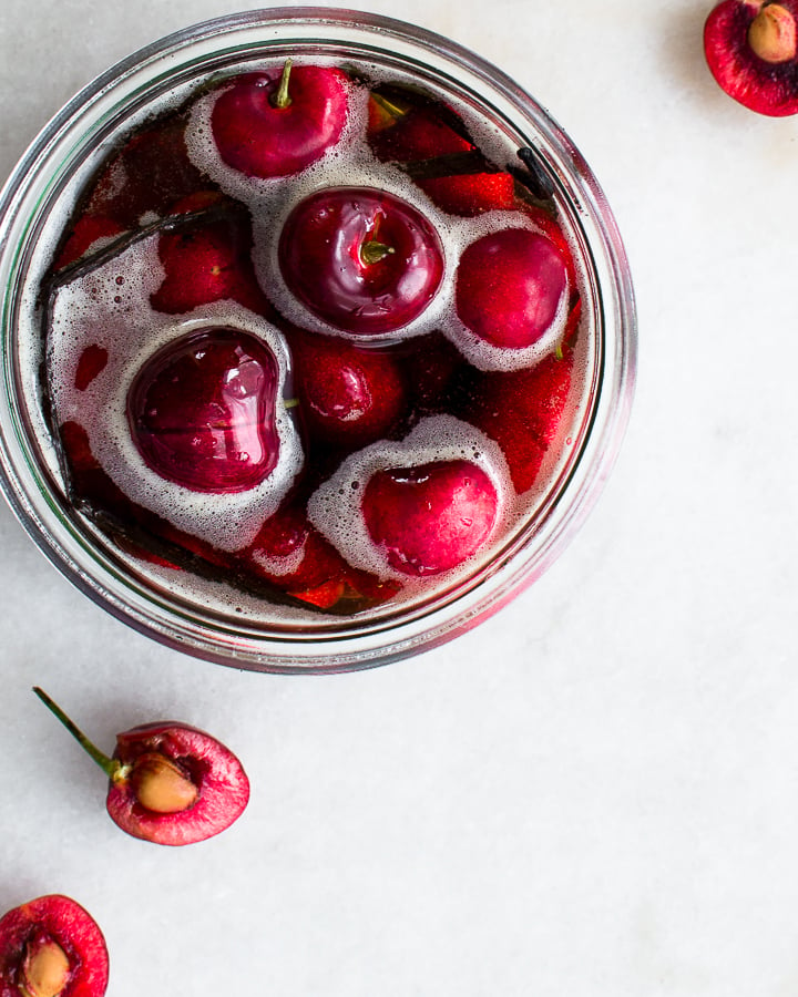 Brandied cherries in a glass jar with a split vanilla bean, ready for storage.