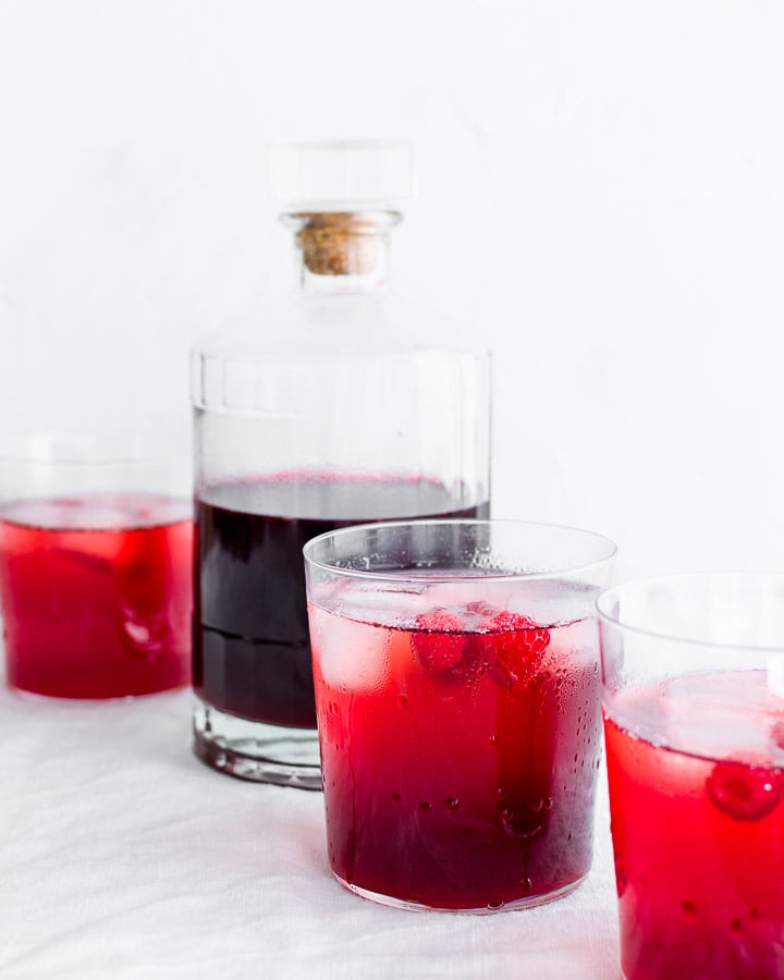 Raspberry shrub in a bottle next to three glasses.