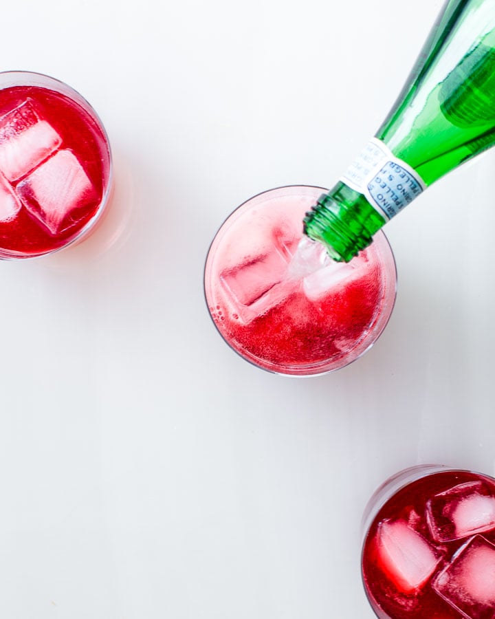 Pouring sparkling mineral water into a glass of raspberry shrub and ice.