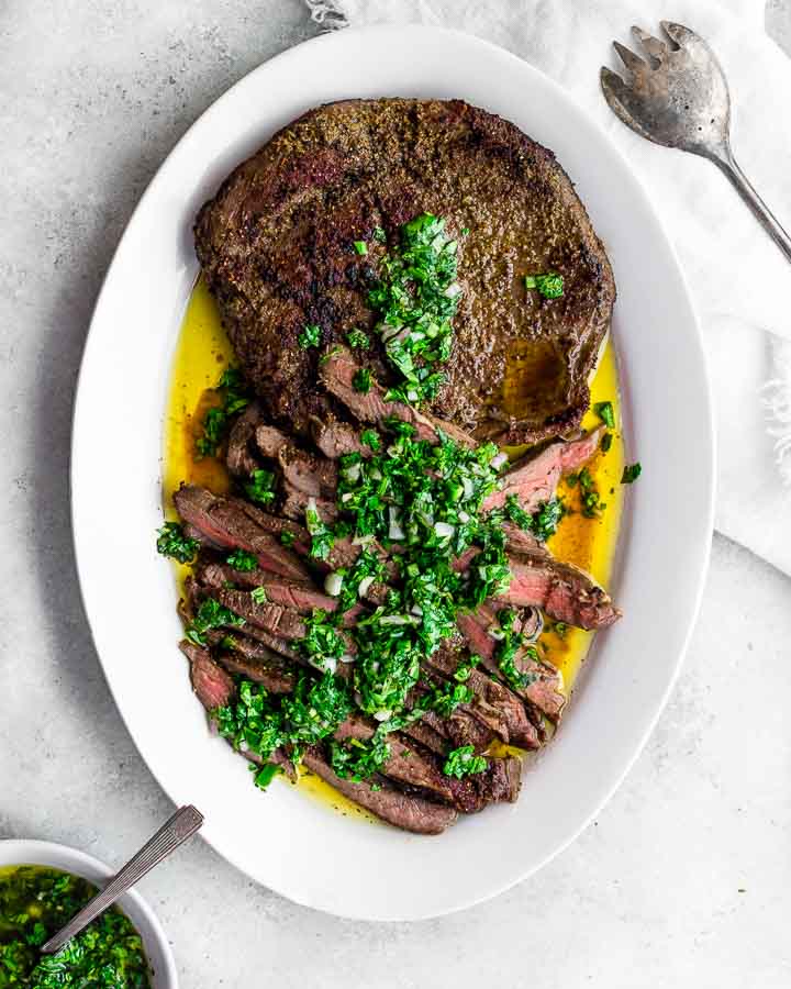 Sous vide flank steak crusted with coriander, cumin and sea salt and served on an oval plate with green herb sauce and extra virgin olive oil.