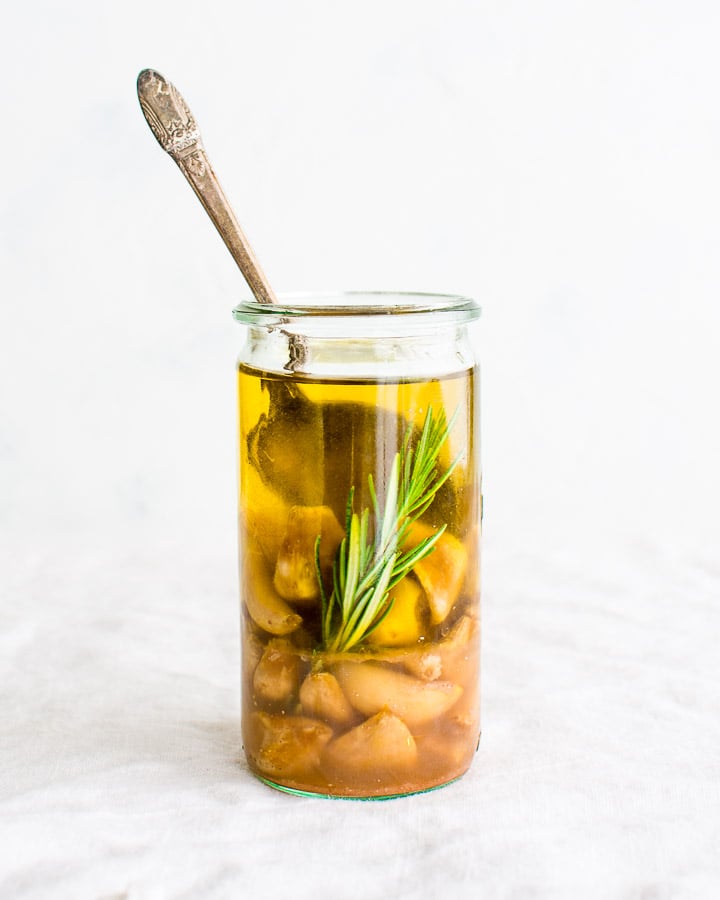 Sous Vide Garlic Confit with Rosemary in a glass jar with a silver spoon.