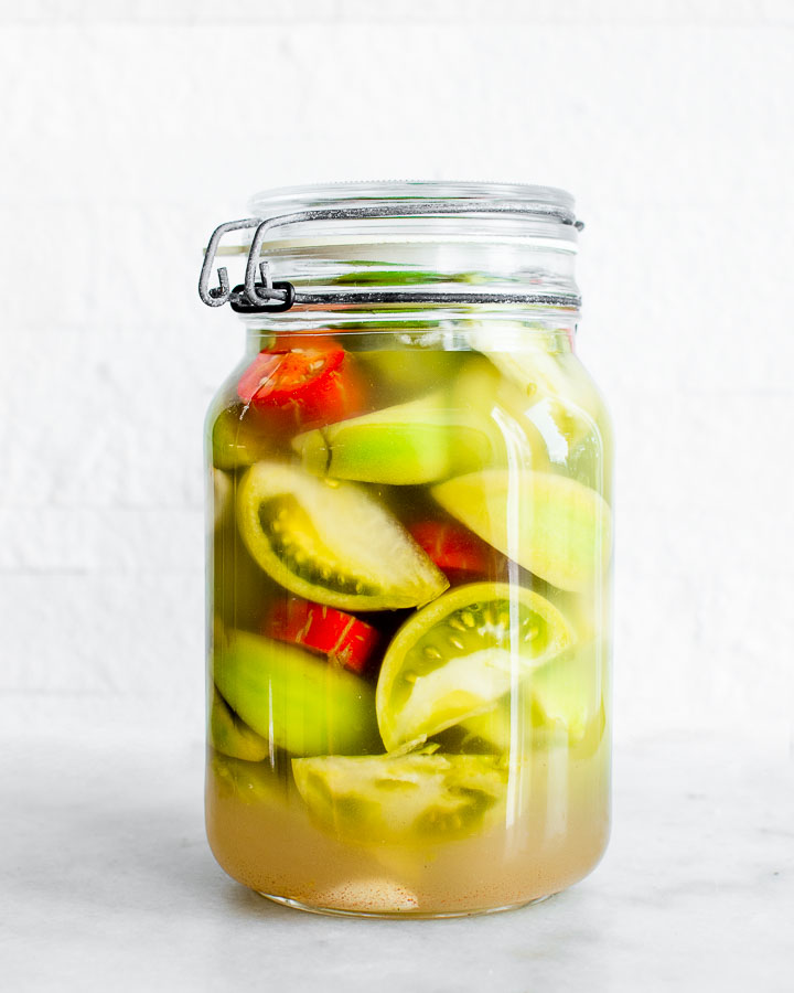 Green tomatoes, red jalapenos and garlic fermenting in a glass jar.