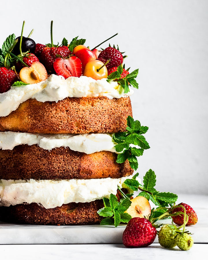 Three-layer almond flour cake topped with whipped cream, cherries, strawberries and mint.