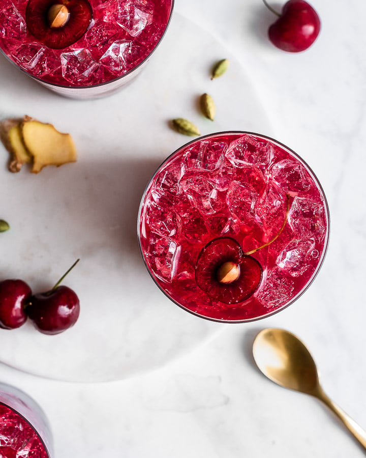 Cherry cordial in a glass of ice shot from overhead, garnished with ginger and cardamom.