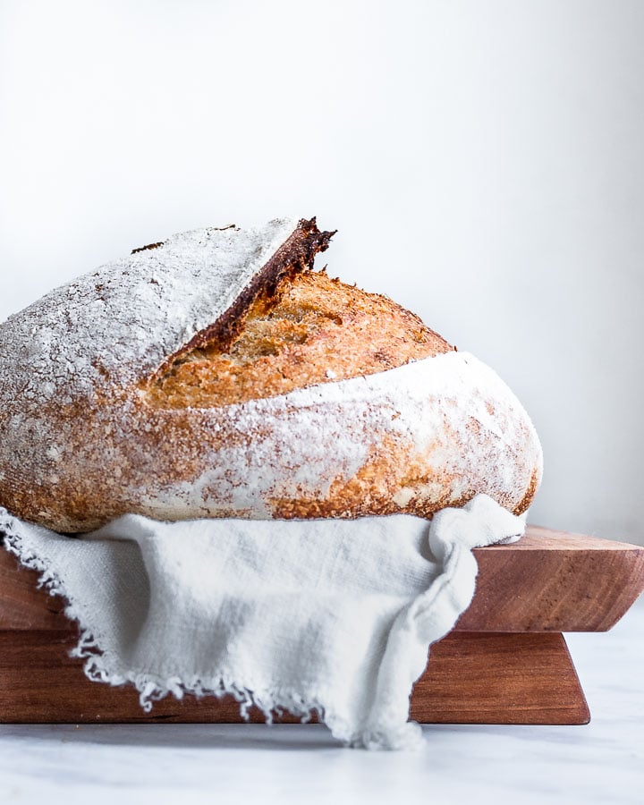 Bread leavened with wild yeast sitting on a linen cloth on a wooden tray.