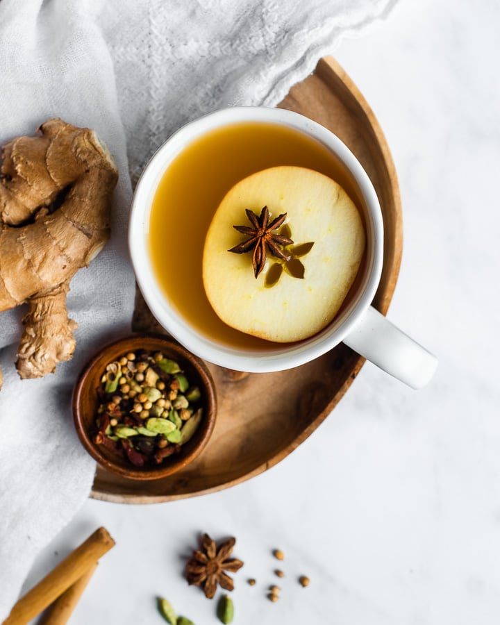 Mug of wassail on a wooden tray, garnished with star anise and sliced apple.