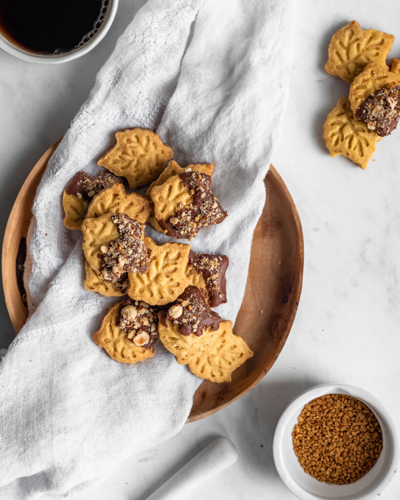 Maple Shortbread cut into leaf shapes and dipped in chocolate on a wooden plate.