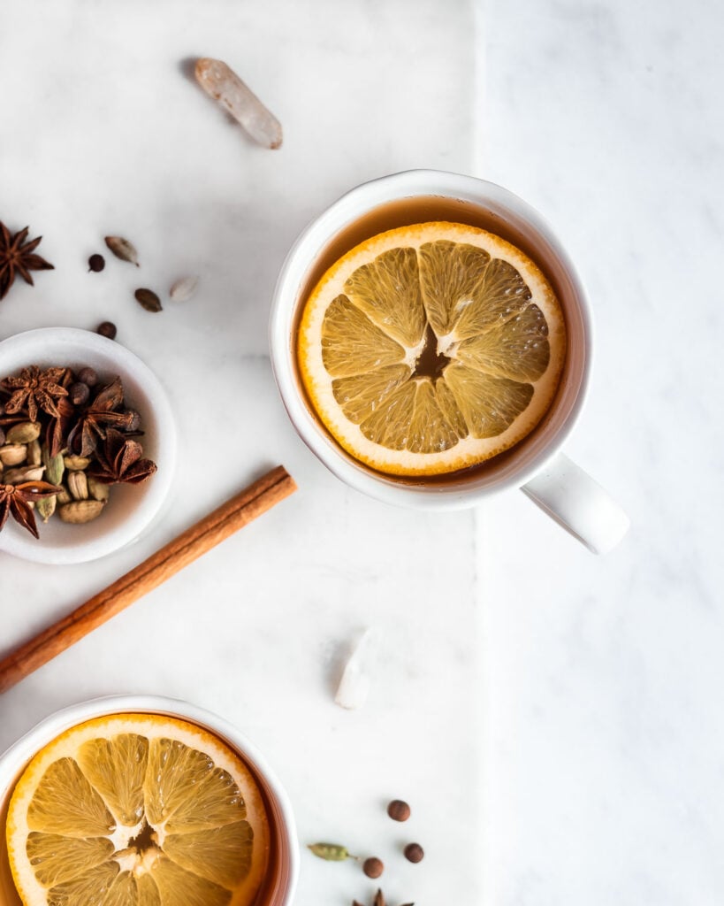 Mulled cider in two white mugs, garnished with orange slices and cinnamon stick