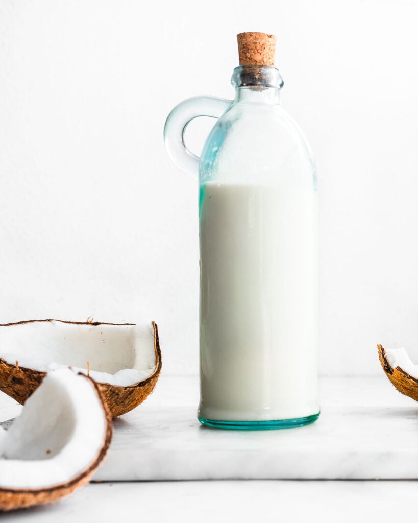 A bottle of homemade coconut milk next to a cracked brown coconut