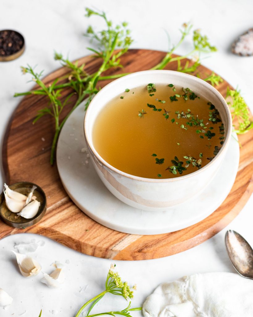 Chicken broth in a bowl, garnished with fresh thyme leaves