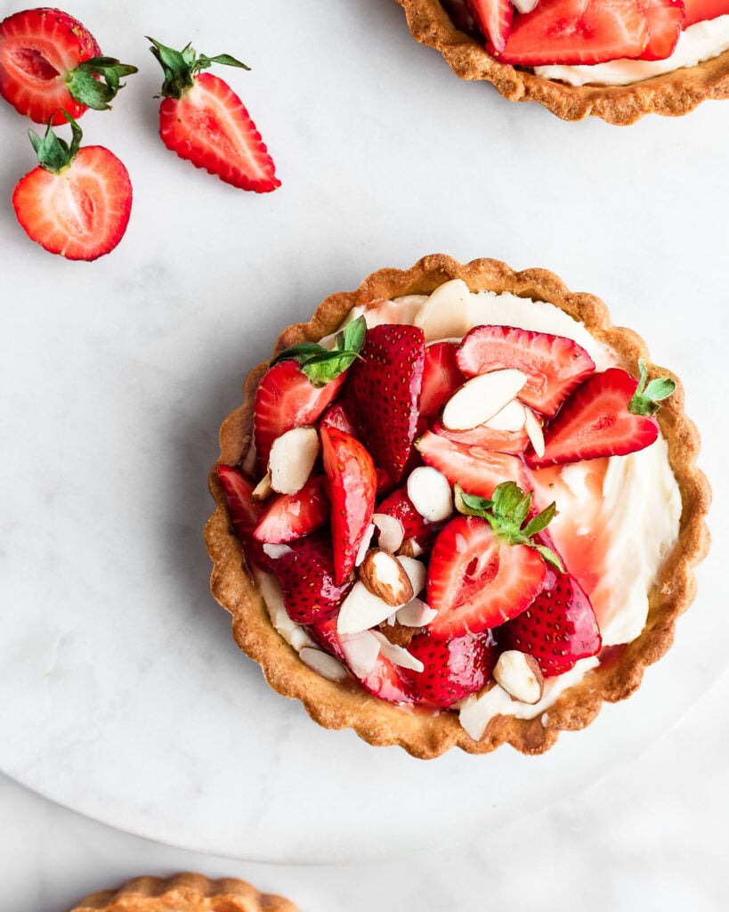 Strawberry tarts on a marble surface, garnished with sliced almonds.