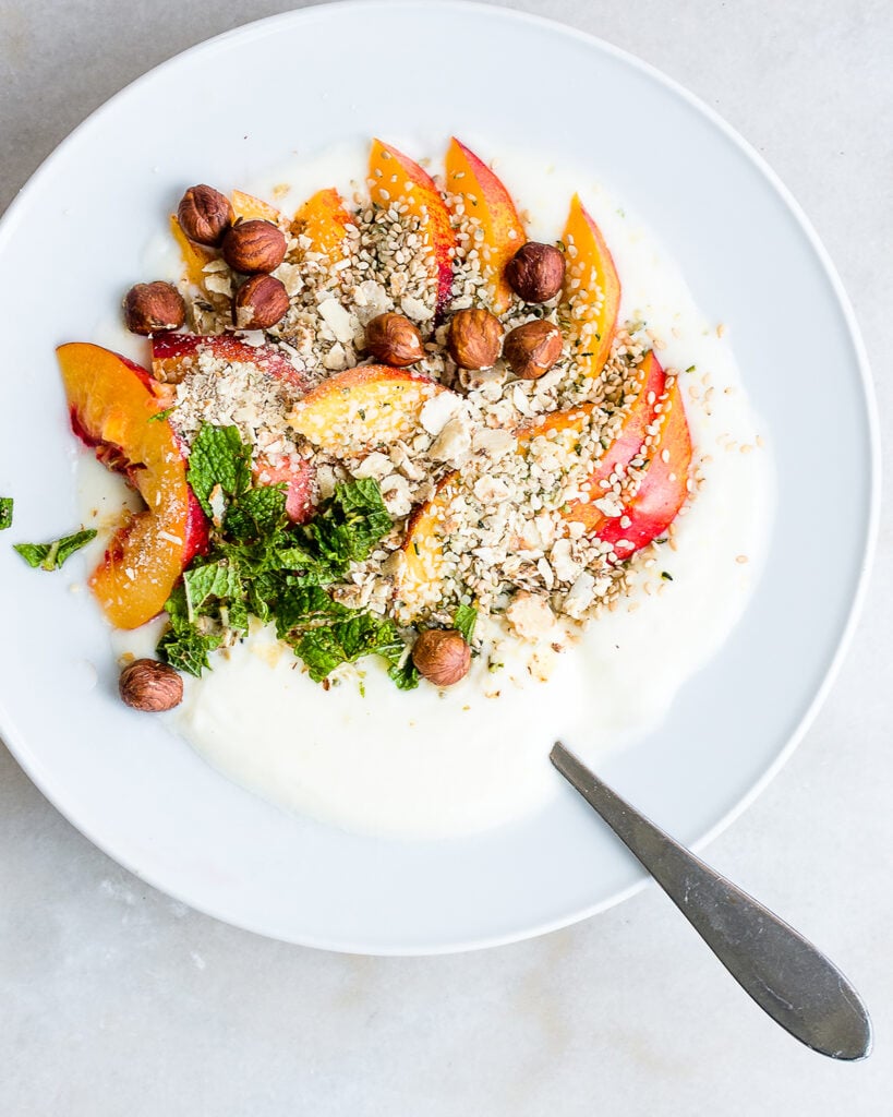 homemade yogurt in a bowl garnished with nectarines, hazelnuts, hemp seeds and mint