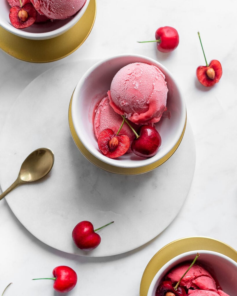 Two scoops of cherry sorbet in a white bowl, garnished with sweet cherries.