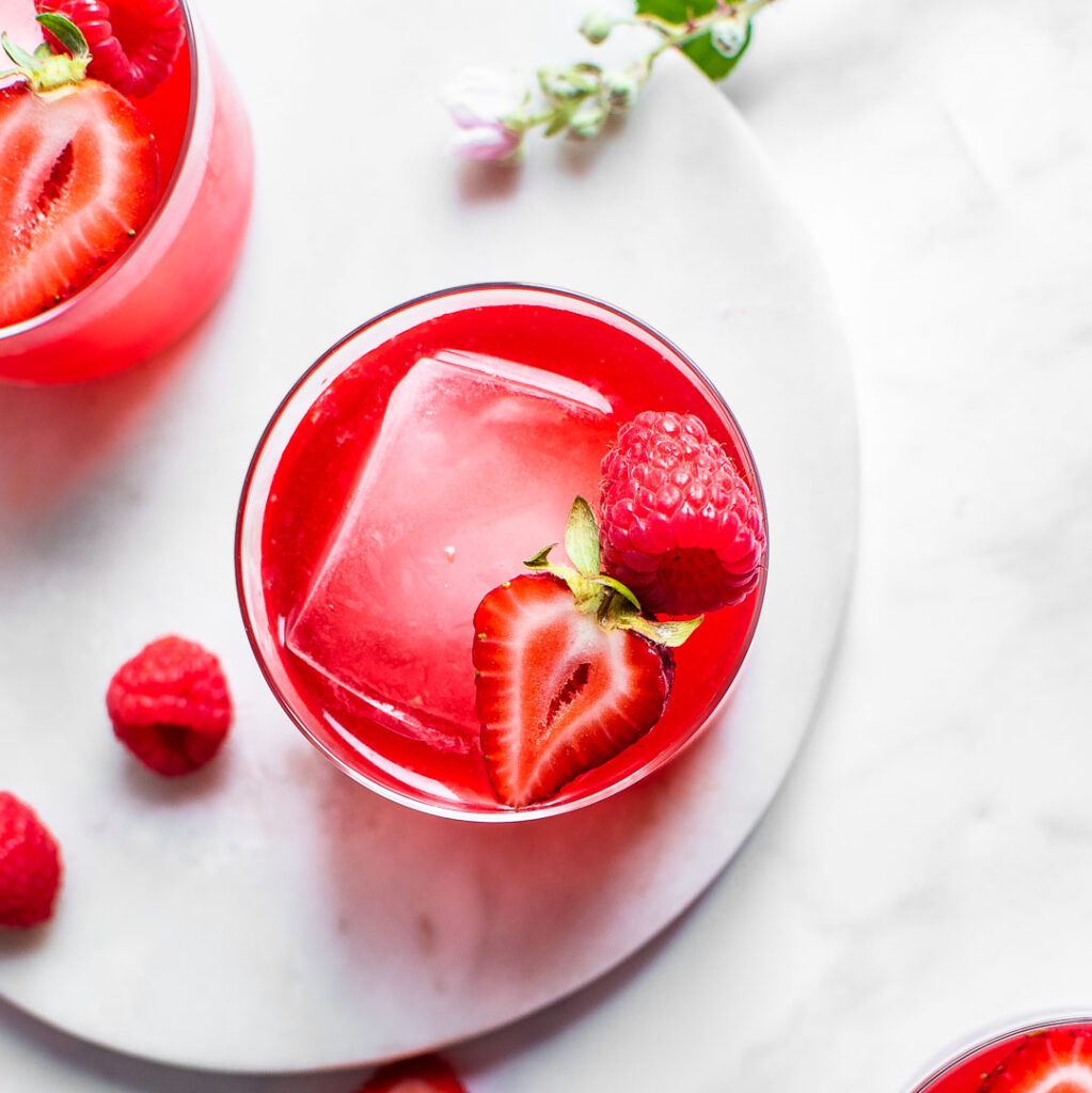 Three glasses of fruit kvass shot from overhead, garnished with ice and strawberries