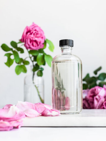 Rose water in a clear bottle with black cap, damask roses in background