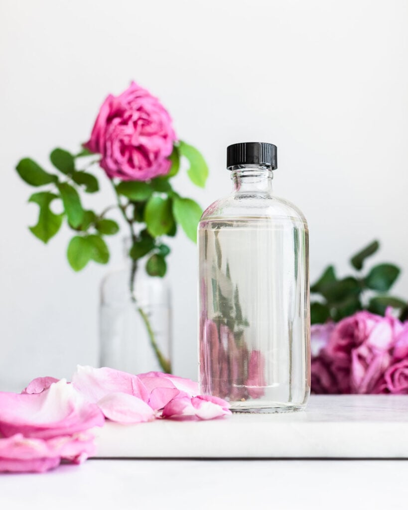 Homemade rose water in a clear glass with pink Damask roses in the background
