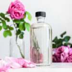 Rose water in a clear bottle with black cap, damask roses in background