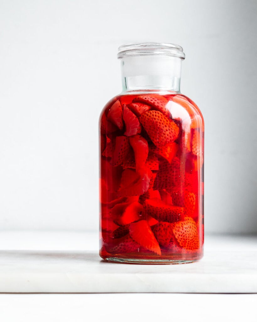 A clear apothecary jar filled with strawberries infusing white wine.