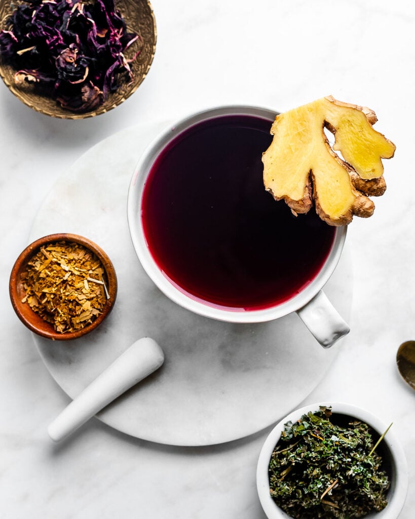 Moon tea in a large white mug, garnished with fresh ginger, red raspberry leaf, and ginkgo