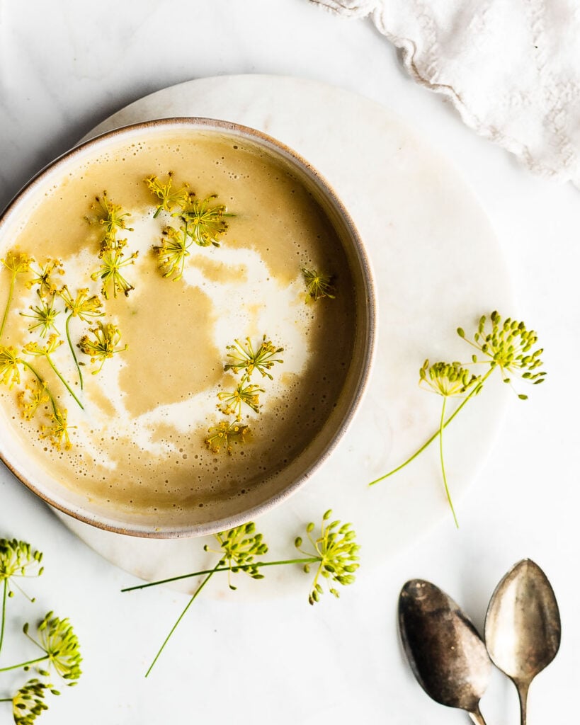 Potato Leek Soup with Dill in an earthenware bowl on a marble surface, garnished with dill flowers and a swirl of heavy cream.