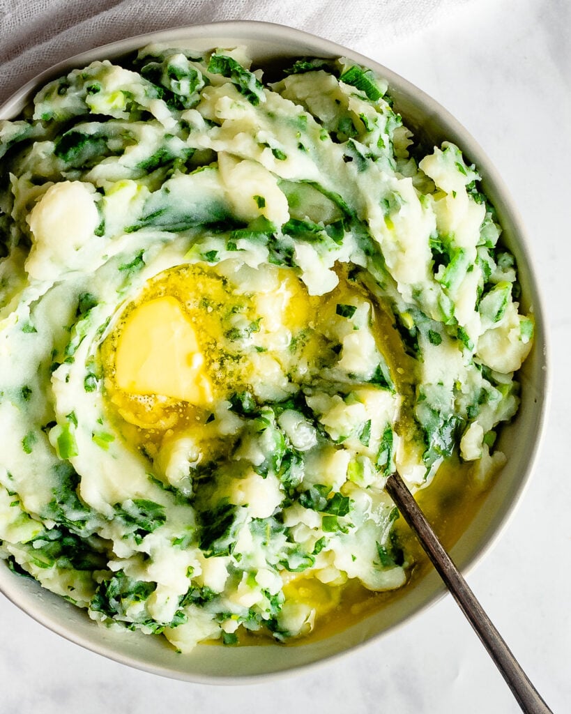 Butter melting in a bowl of colcannon made with kale, potatoes, and green onions.