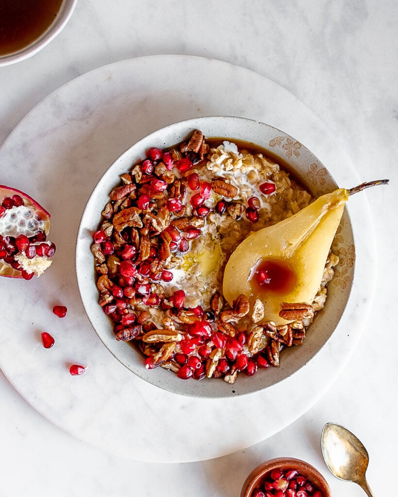 soaked oatmeal porridge in a bowl, garnished with pecans, pomegranate seeds and poached pear