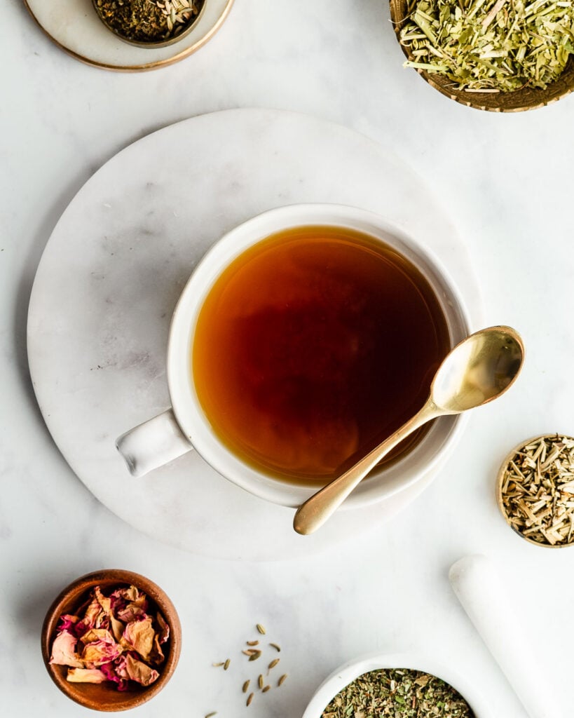 Herbal tea in a white mug with a golden spoon next to small bowls filled with passionflower and rose slightly out of frame