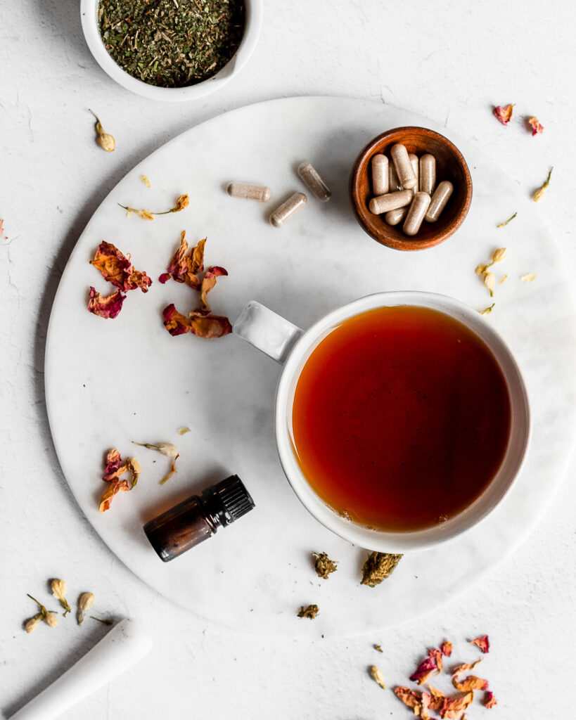 Mug of tea on a white marble surface, along with herbs, supplements and essential oils