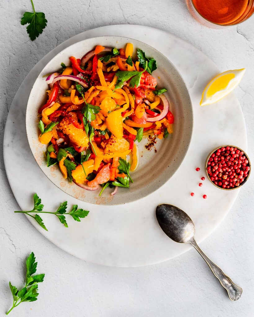 Bell Pepper Salad on an earthenware plate next to a lemon wedge and pinch bowl filled with pink peppercorns