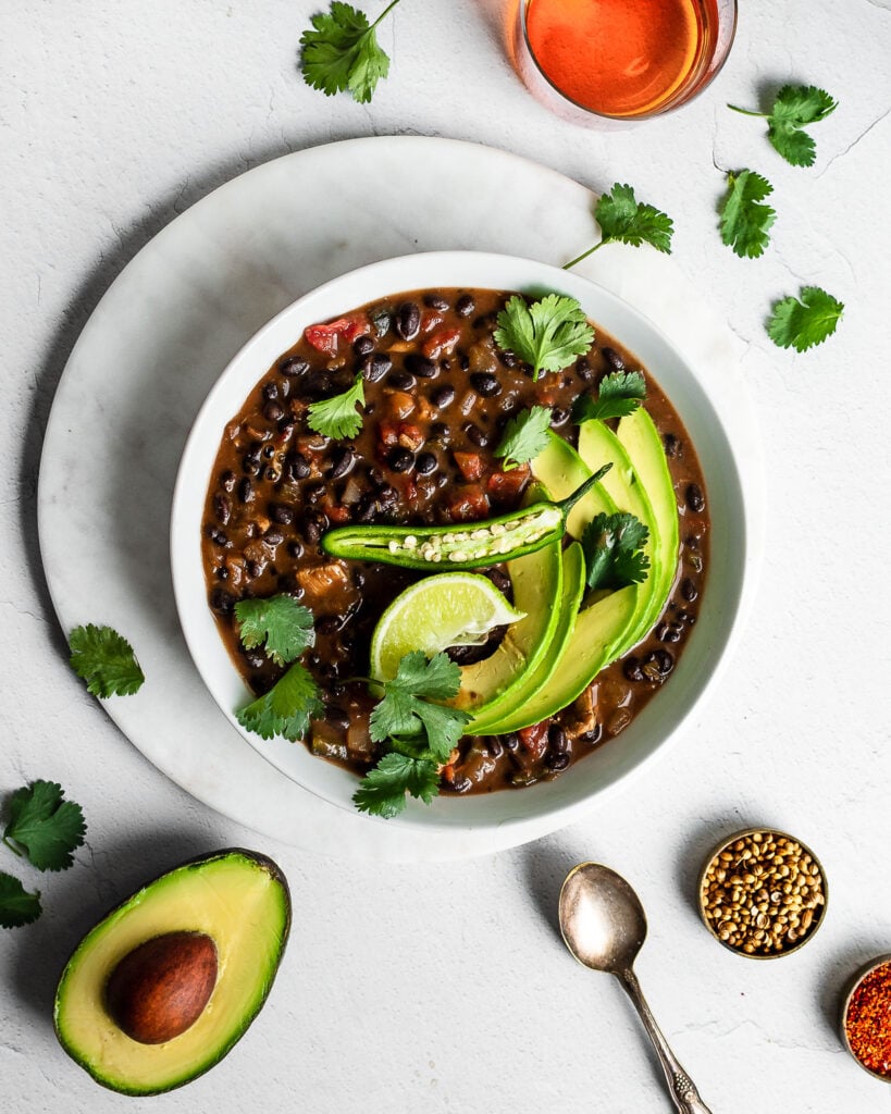 Black bean soup with chicken in a bowl, garnished with cilantro, lime, avocado and serrano chili