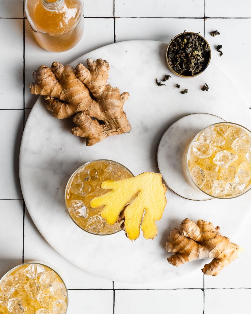 ginger kombucha in glasses of ice garnished with fresh ginger