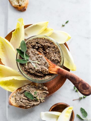 Mushroom pate in a glass jar on a copper dish garnished with sage leaves and fresh thyme, served with toasted bread and Belgian endive